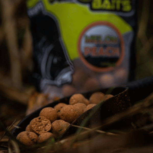 Boilies Melon & Peach – Cebo saliendo del paquete Pro Elite Baits sobre fondo natural